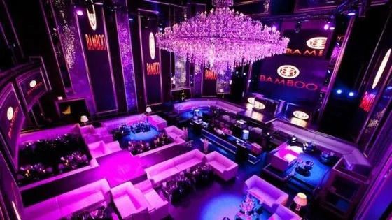 Nightclub main room with chandelier and banquette seating under coloured lighting