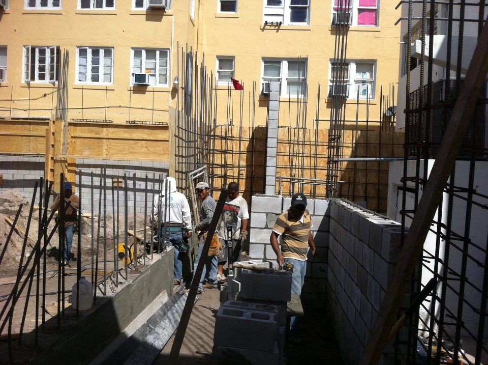 Masons laying concrete block with vertical rebar beside an existing apartment building