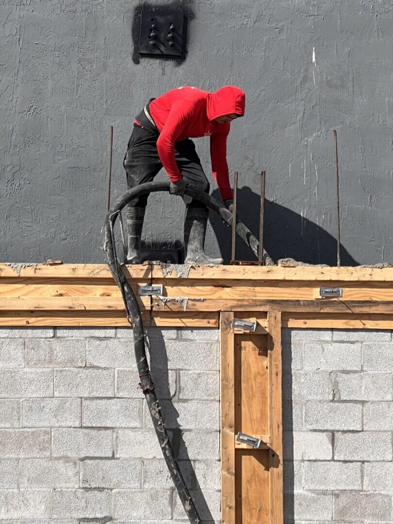 Worker placing concrete into a tie beam form on top of a block wall