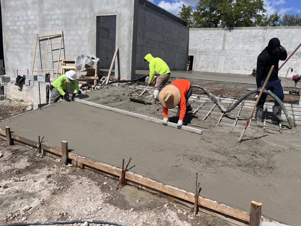 Four-man crew screeding a freshly poured concrete slab inside block walls
