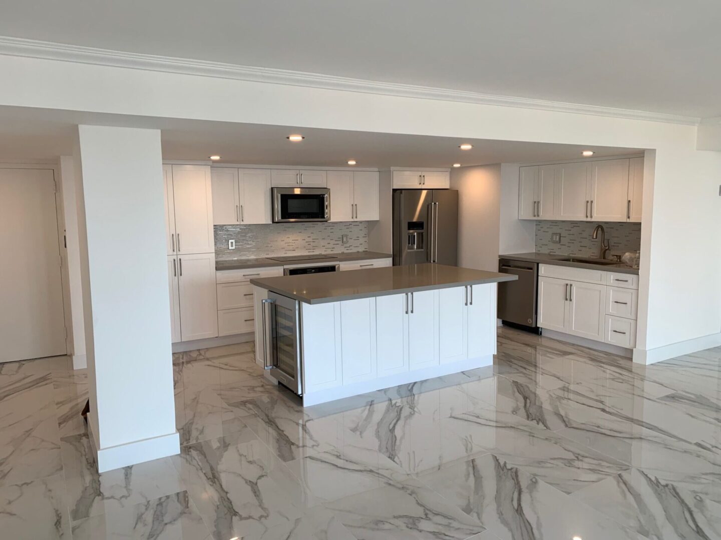 A kitchen with white cabinets and marble floors.