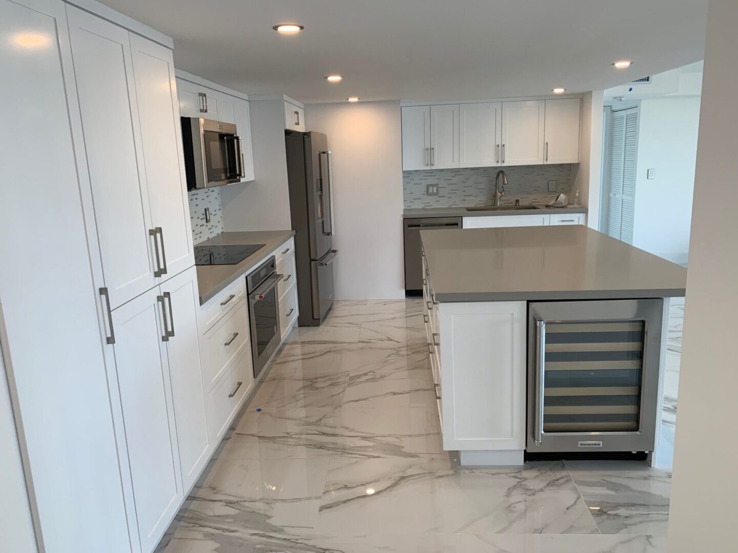 A kitchen with white cabinets and marble floors.
