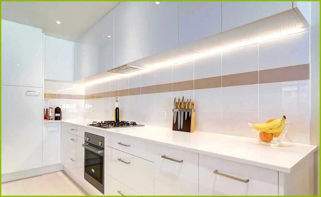 A kitchen with white cabinets and lights on the wall.